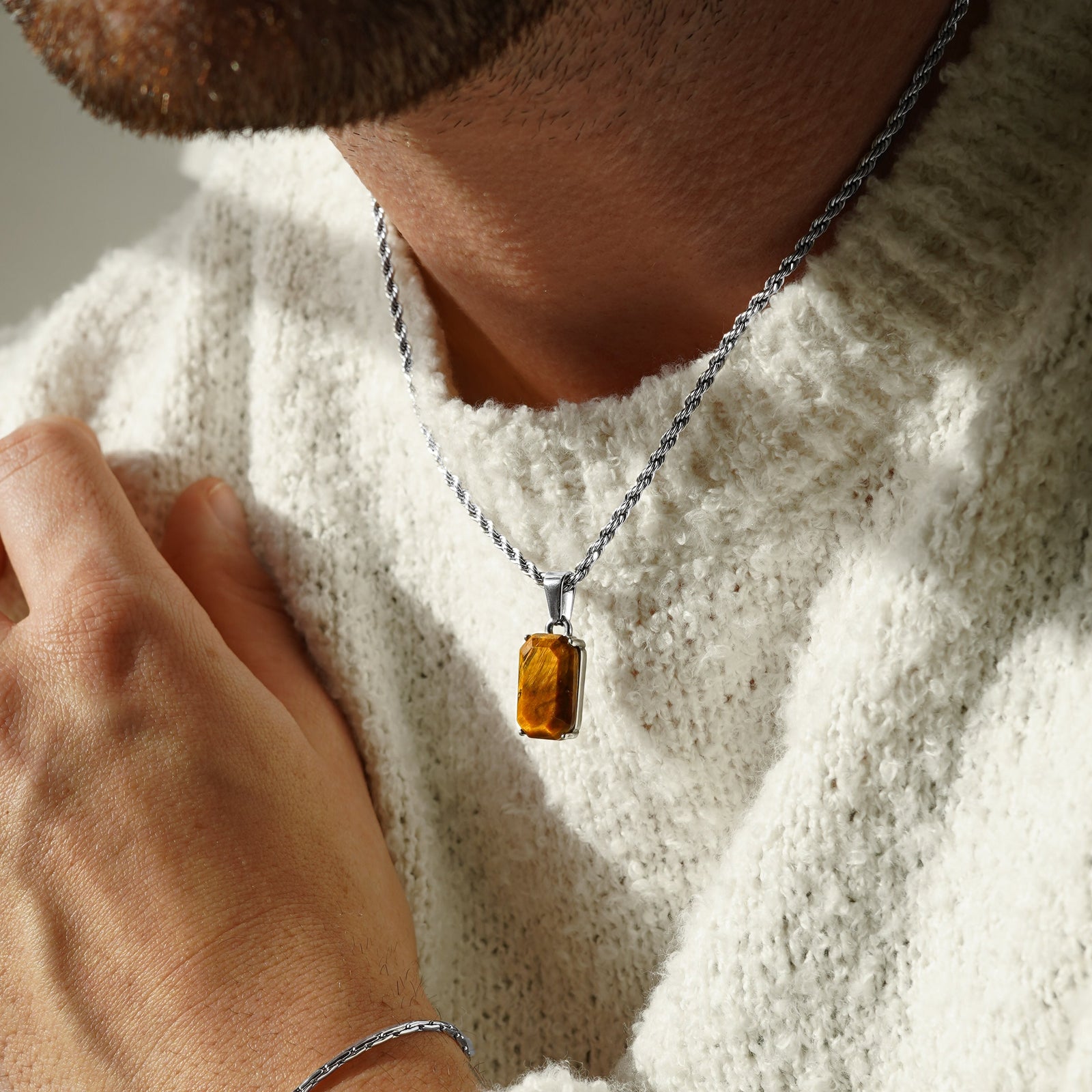 Person wearing a tigers eye necklace with a amber pendant and a bracelet on a light background