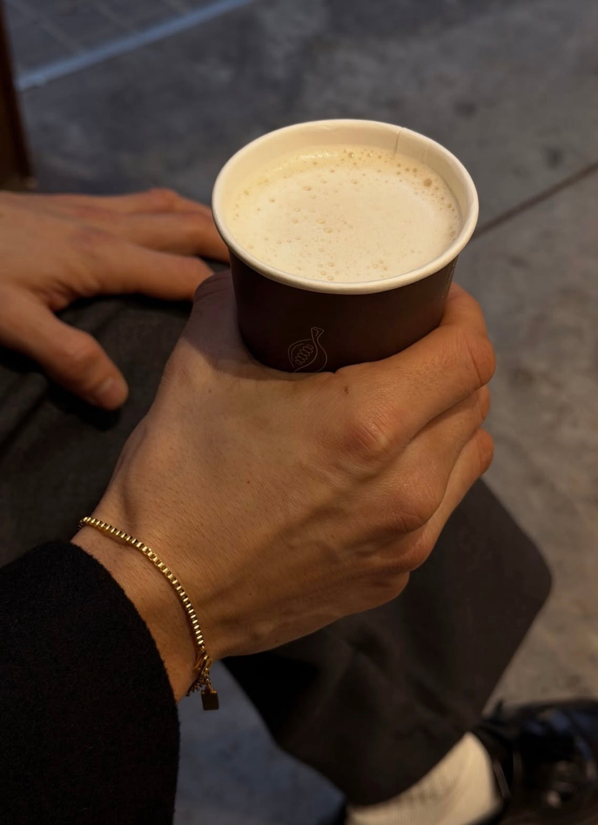 Gold box chain bracelet worn on wrist while holding a coffee cup in a casual lifestyle setting