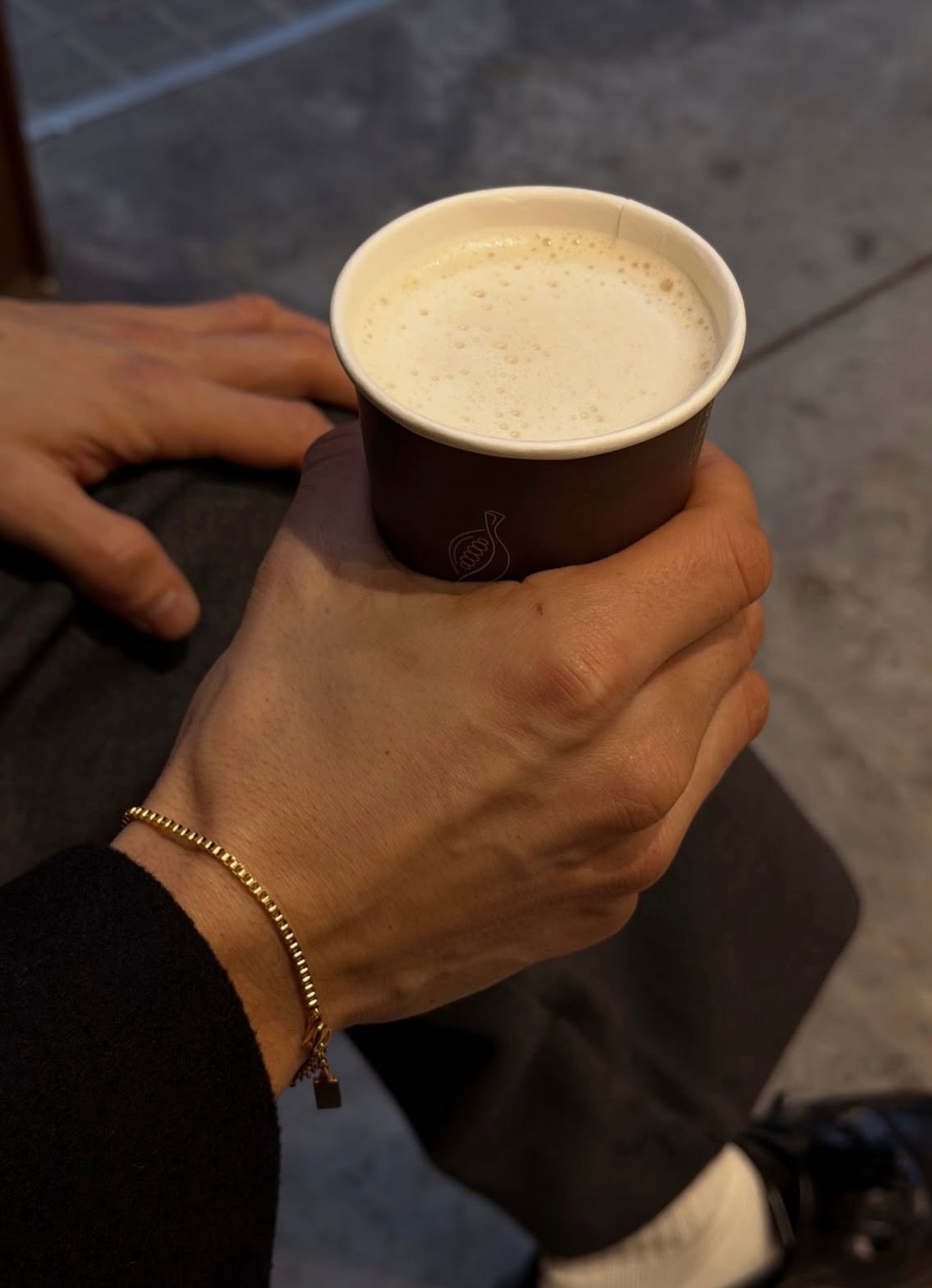 Gold box chain bracelet worn on wrist while holding a coffee cup in a casual lifestyle setting