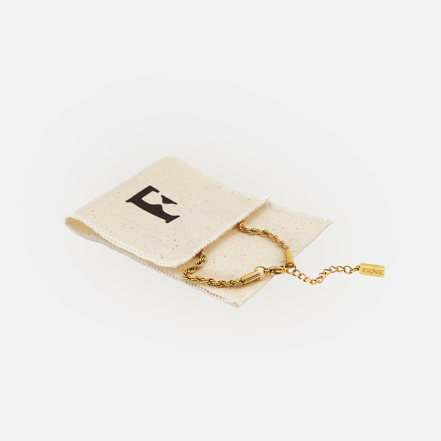 Gold chain bracelet by FRNE placed on branded cotton storage pouch on a white background