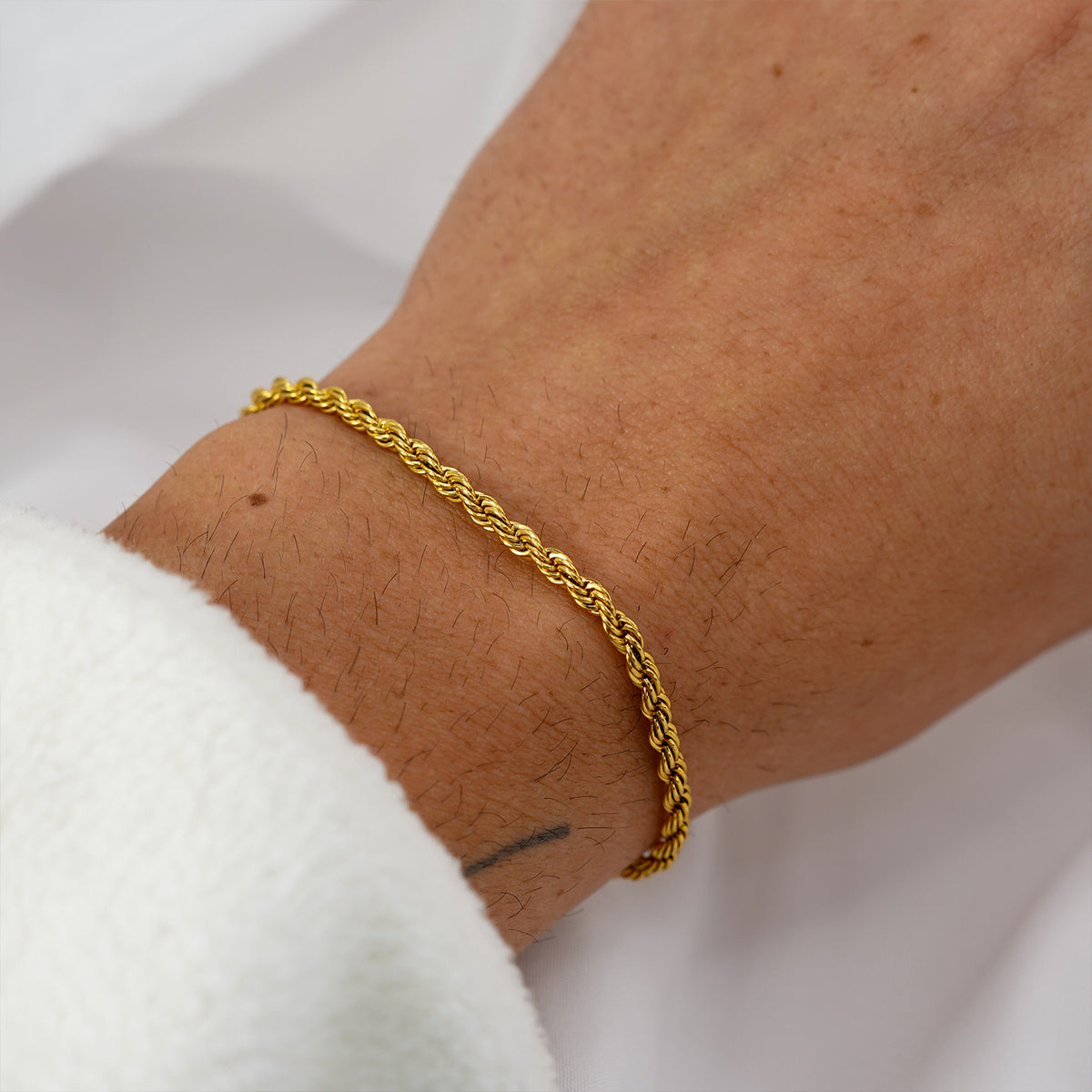 Close-up of gold rope bracelet worn on wrist with soft white background