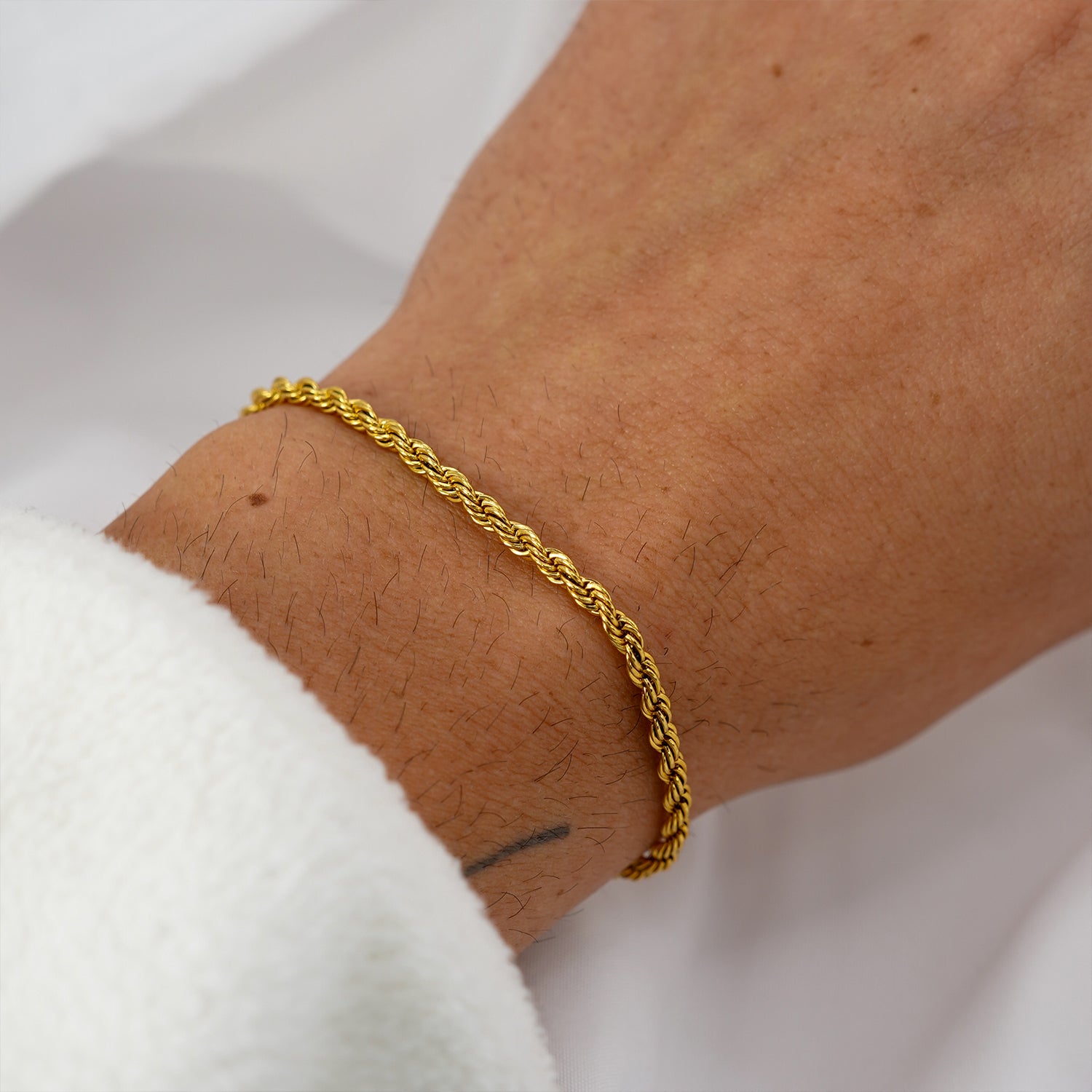 Close-up of gold rope bracelet worn on wrist with soft white background