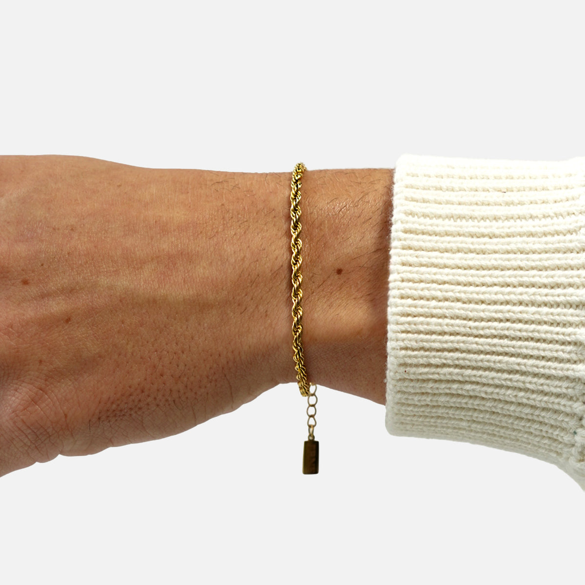 Gold rope bracelet with extension chain and tag worn on wrist with white sleeve