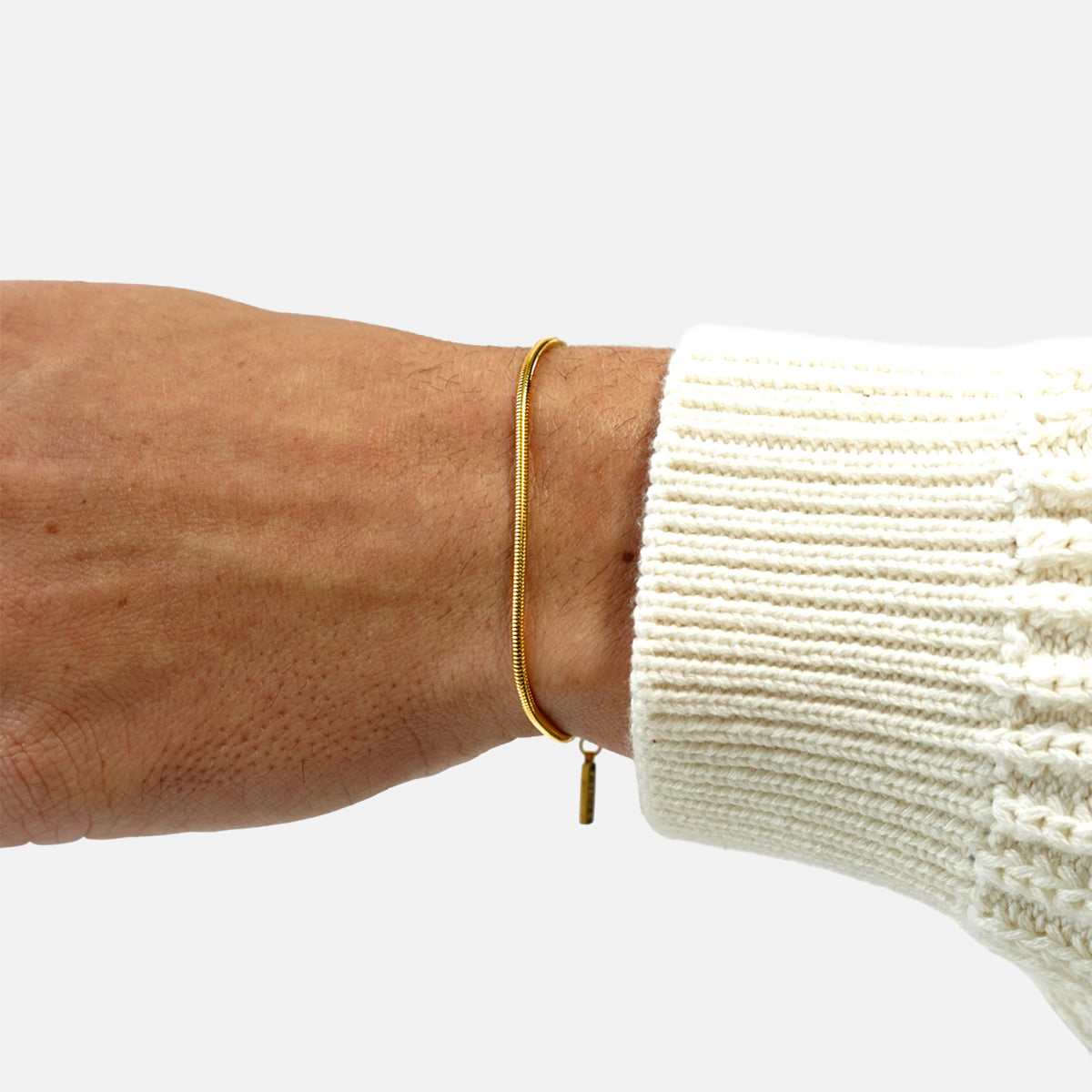 Gold snake chain bracelet by FRNE worn on wrist with white sleeve on a white background