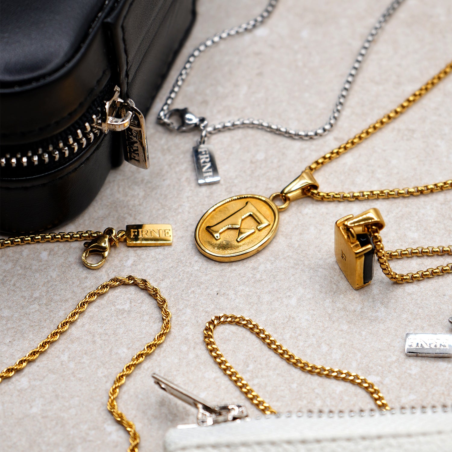 Gold and silver necklaces on a textured surface with a black bag and white box.