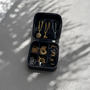 Black jewelry case with gold and silver necklaces on a textured surface