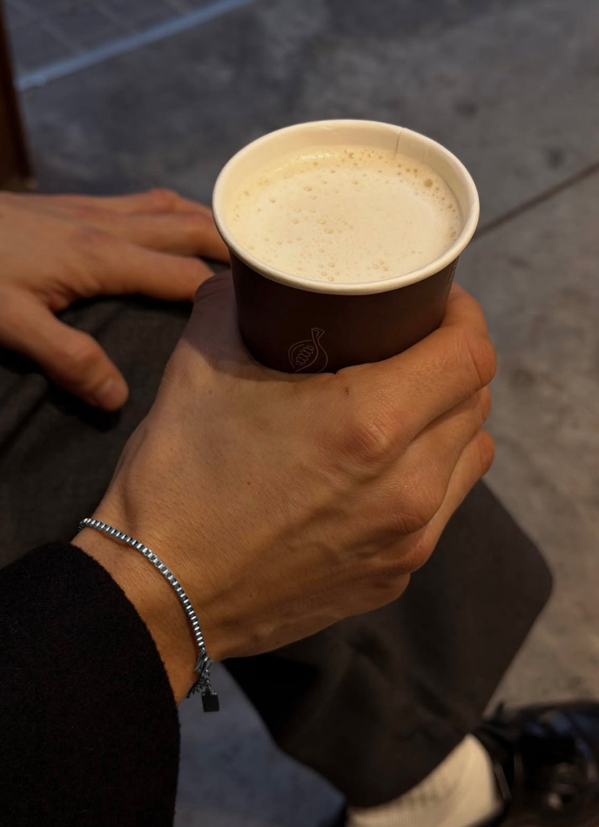 Silver box chain bracelet worn on wrist holding coffee cup in lifestyle setting