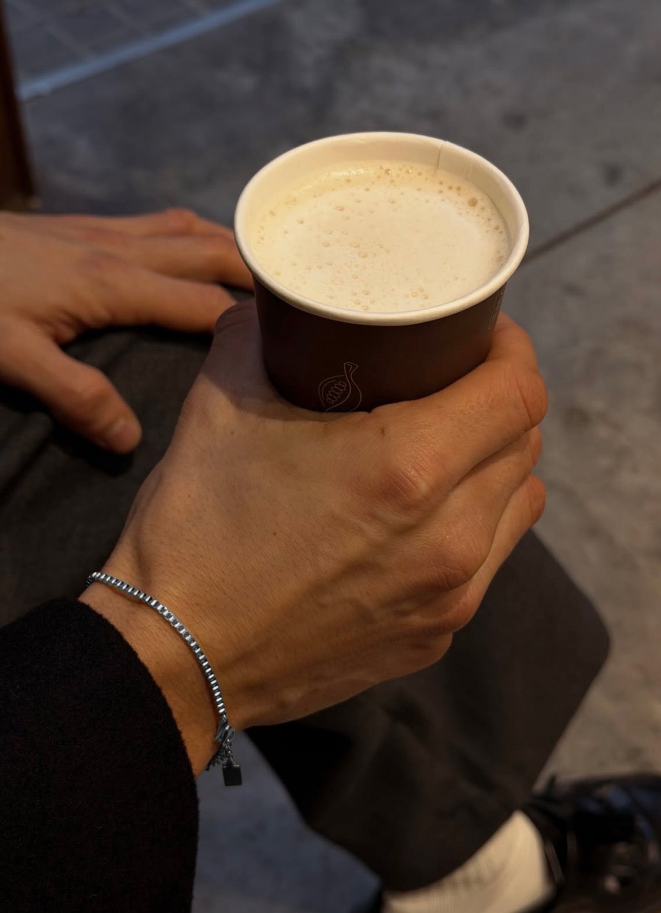 Silver box chain bracelet worn on wrist holding coffee cup in lifestyle setting