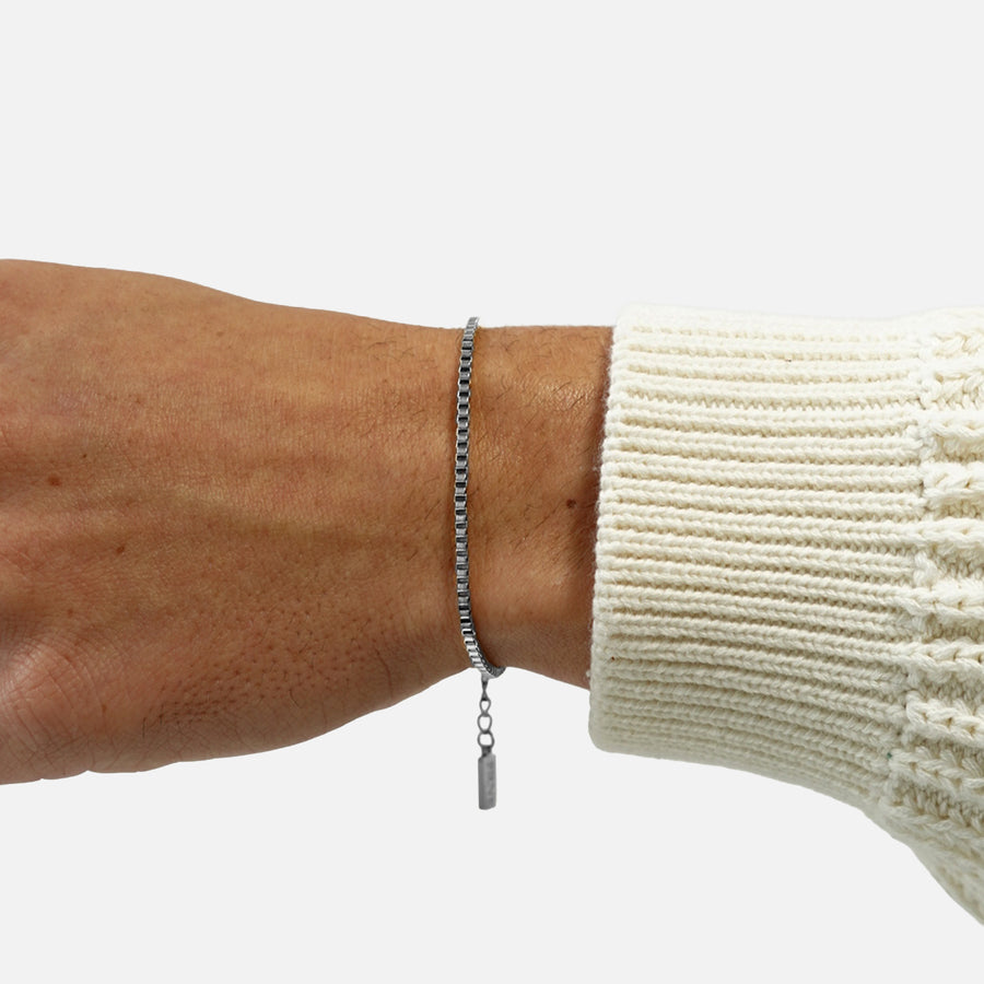 Silver box chain bracelet worn on wrist with extension chain detail on white background