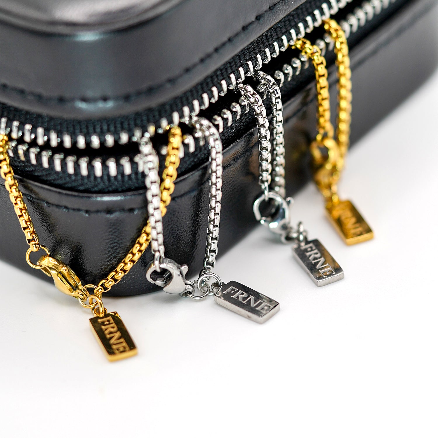 Gold and silver necklaces with 'FRNE' charms on a black zippered case.