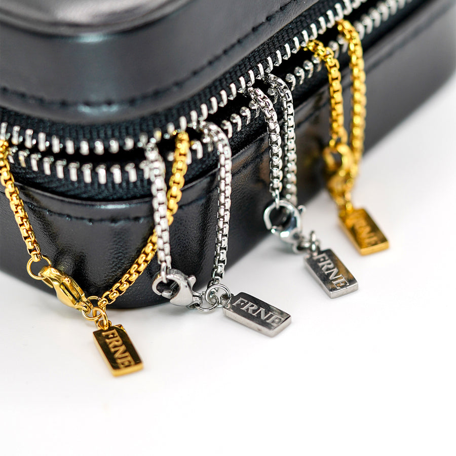 Gold and silver necklaces with 'FRNE' charms on a black zippered case.