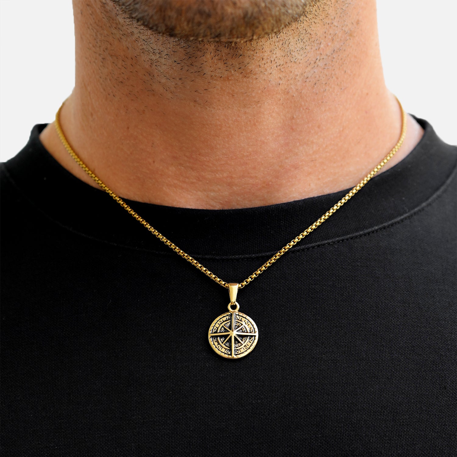 Gold necklace with a compass pendant worn by a person on a black shirt background