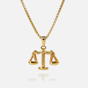 Gold necklace with a Libra scale pendant on a white background