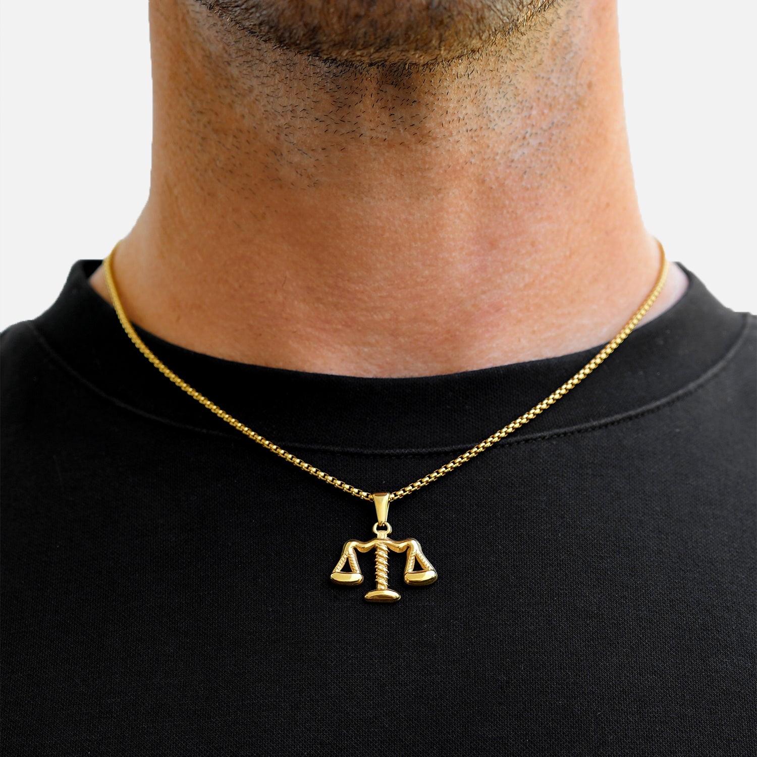 Gold necklace with a scale pendant worn by a person on a plain background