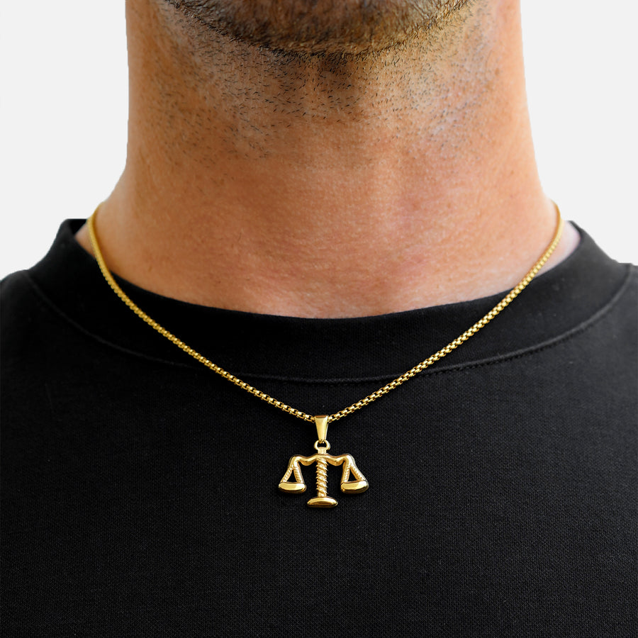 Gold necklace with a scale pendant worn by a person on a plain background