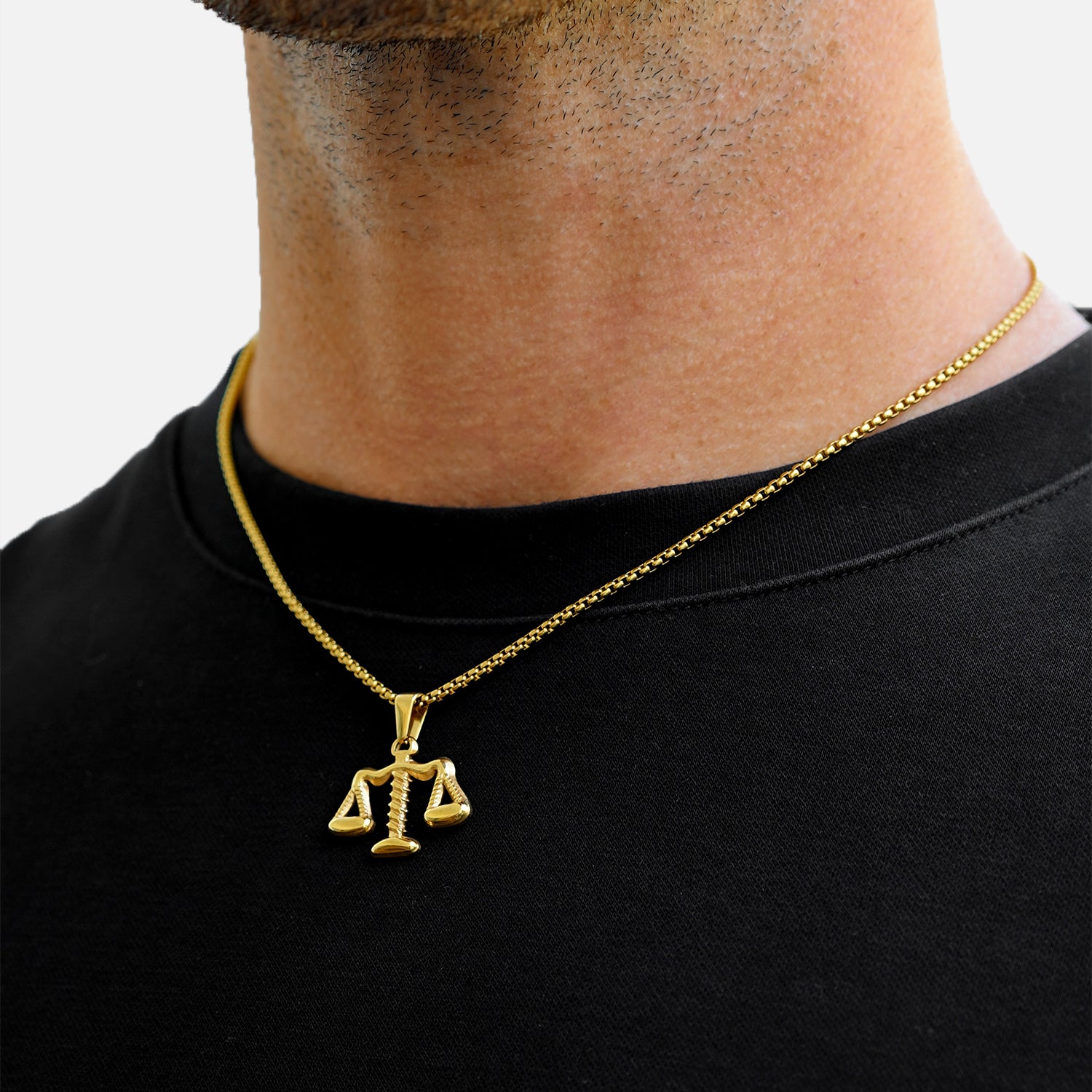 Gold necklace with a scale pendant worn by a person on a black shirt.