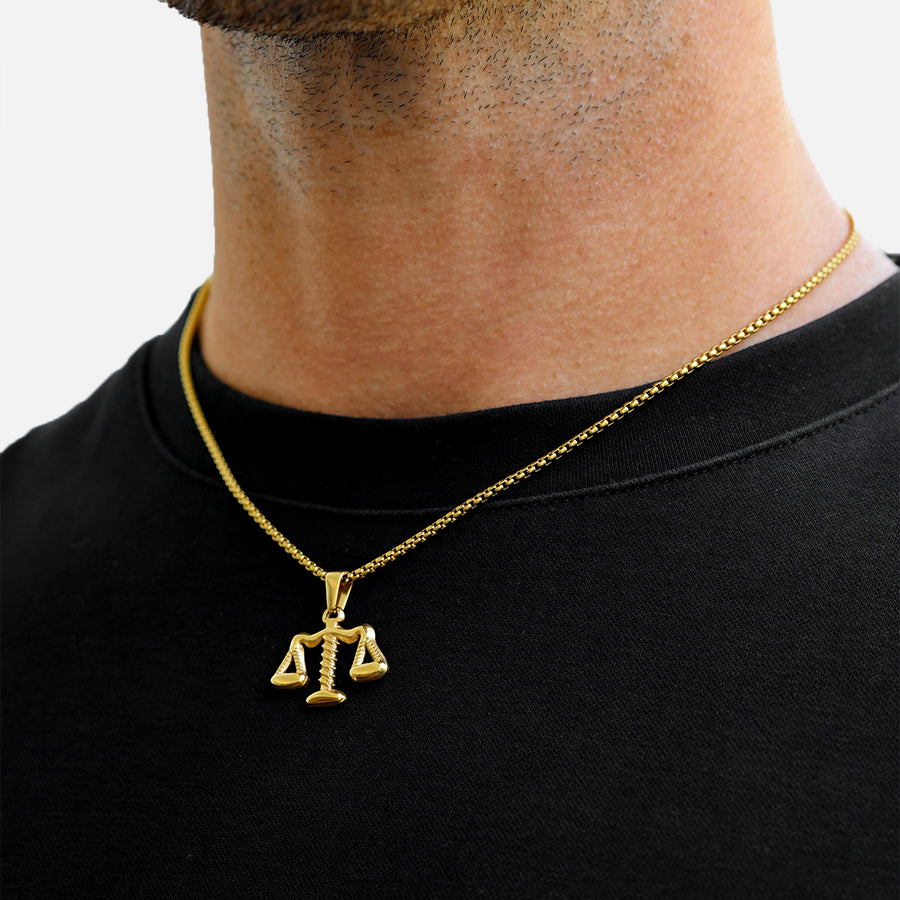 Gold necklace with a scale pendant worn by a person on a black shirt.