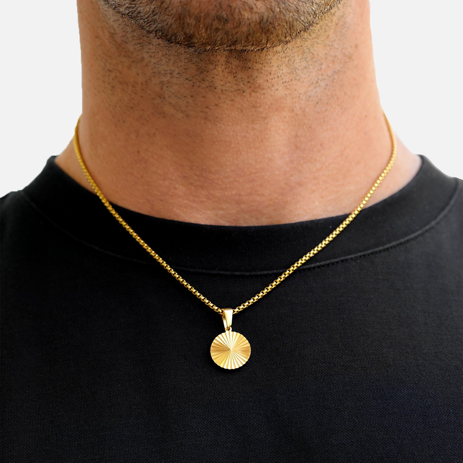 Gold necklace with a round pendant worn by a person on a plain background