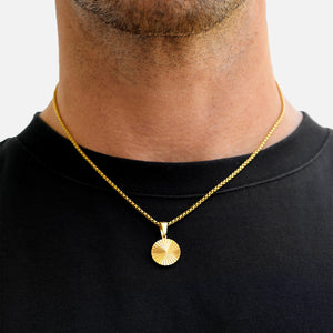 Gold necklace with a round pendant worn by a person on a plain background