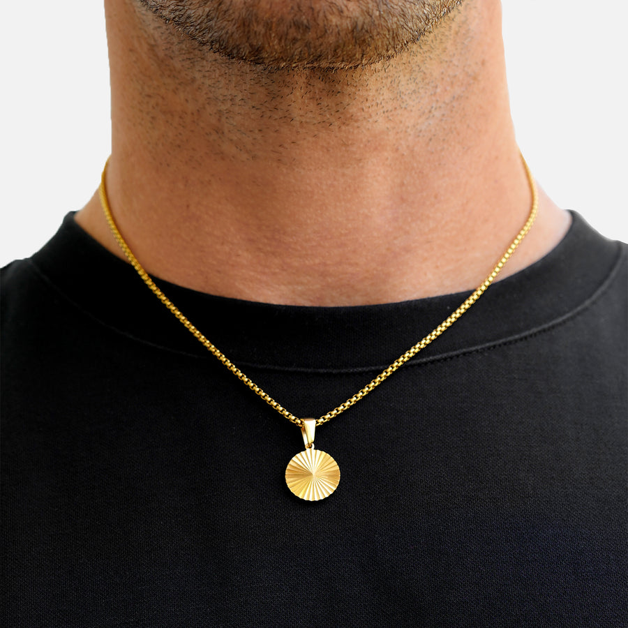 Gold necklace with a round pendant worn by a person on a plain background