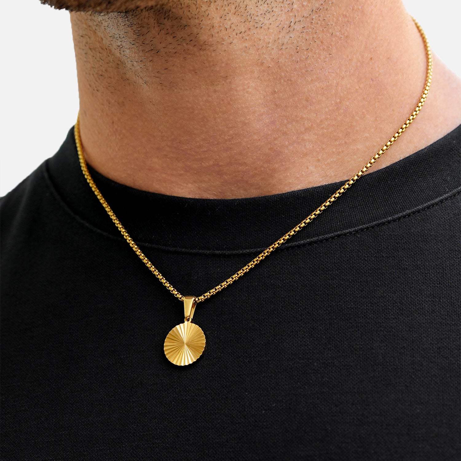 Gold necklace with a pendant on a person wearing a black shirt against a white background
