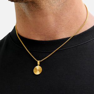Gold necklace with a pendant on a person wearing a black shirt against a white background
