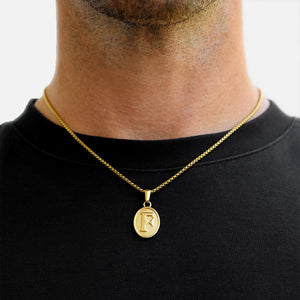 Gold necklace with a pendant worn by a person on a plain background