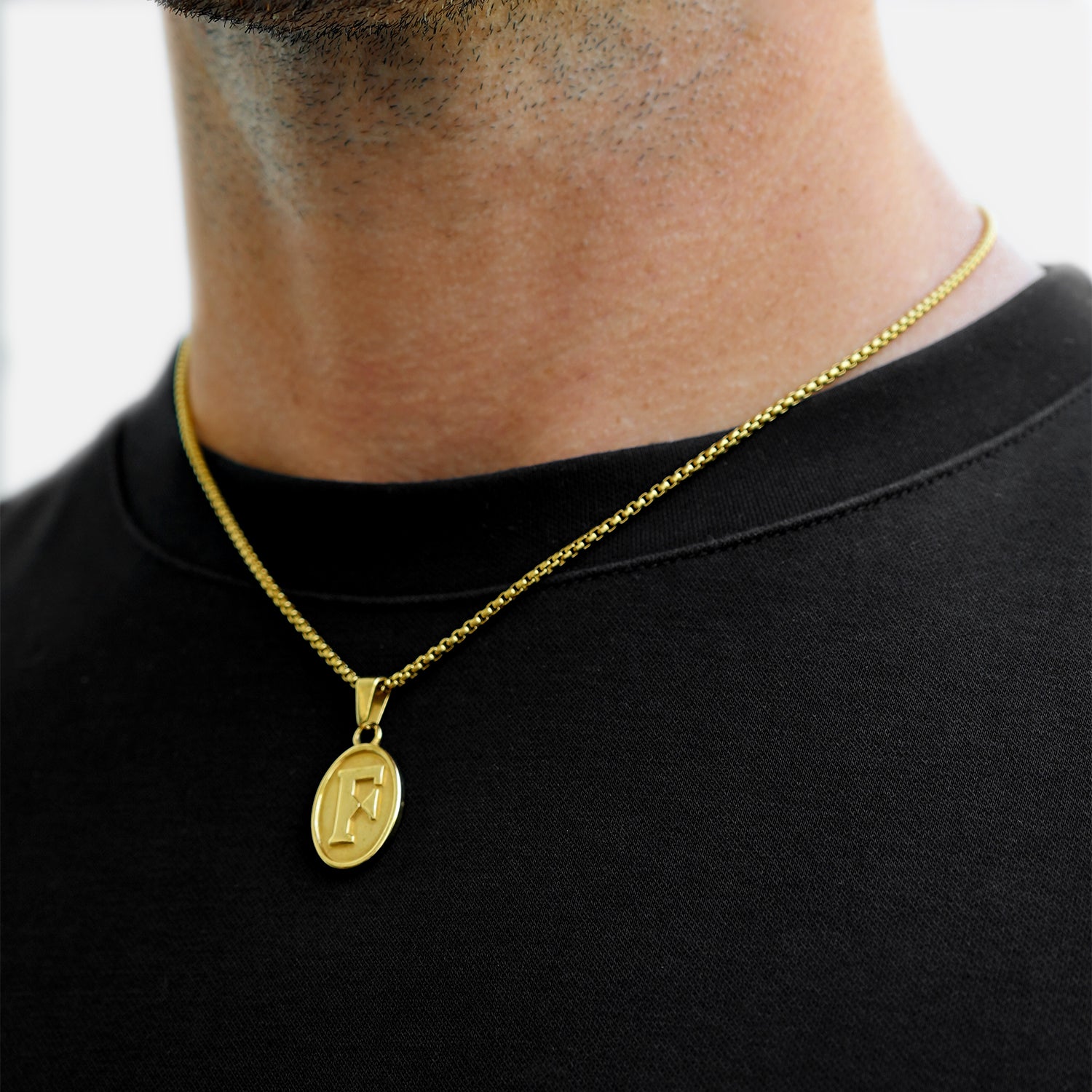 Gold necklace with a pendant on a person wearing a black shirt.