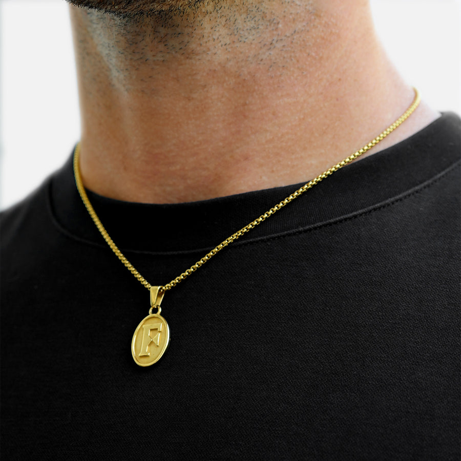 Gold necklace with a pendant on a person wearing a black shirt.