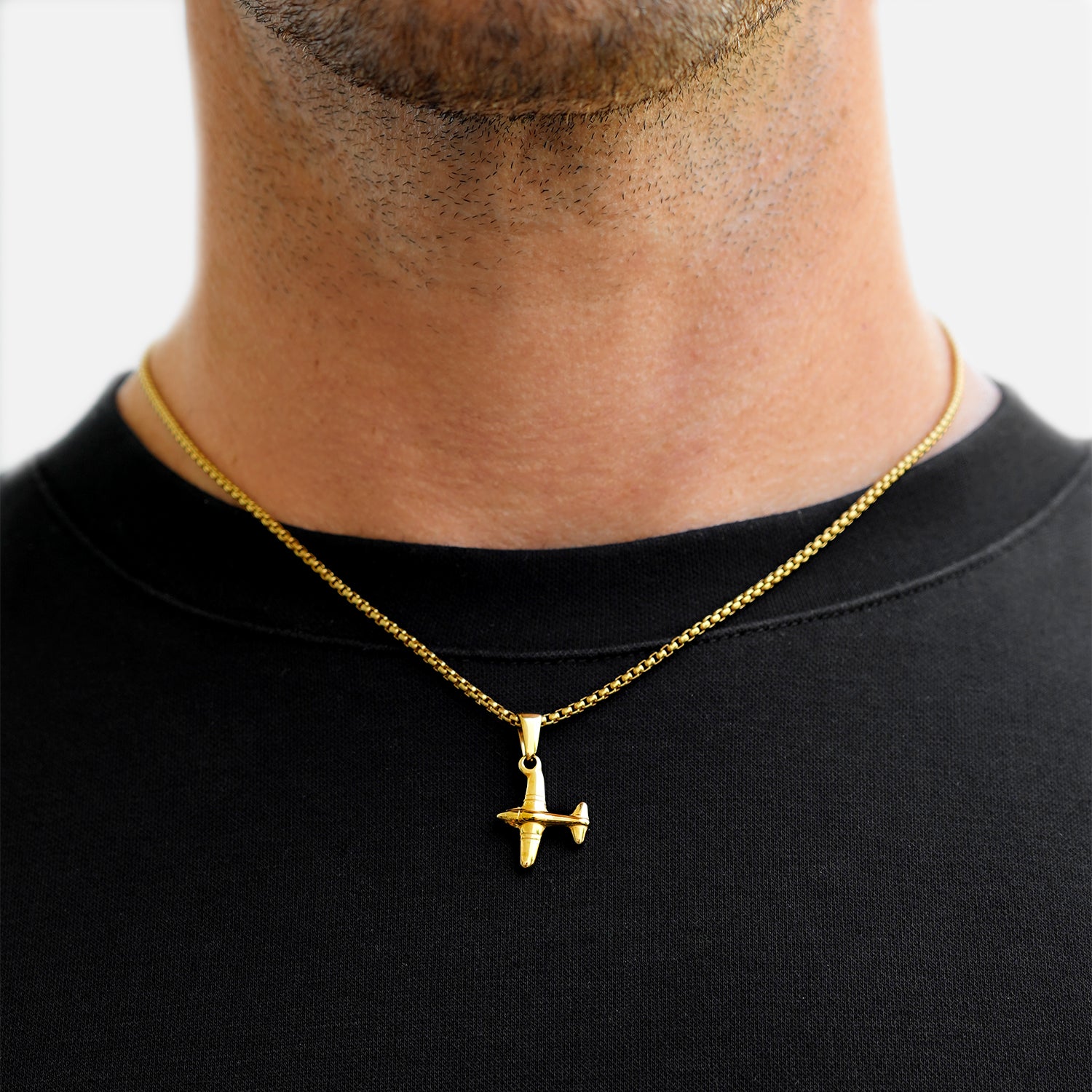 Gold airplane pendant necklace on a black shirt against a neutral background