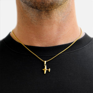Gold airplane pendant necklace on a black shirt against a neutral background