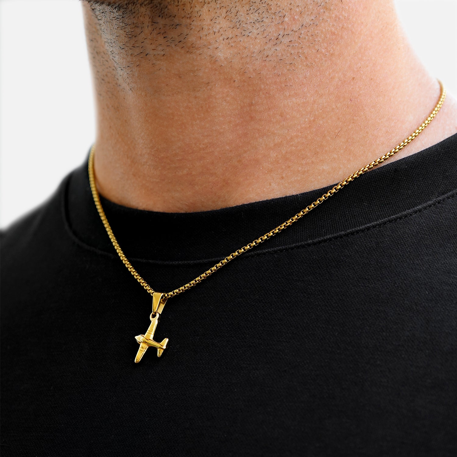 Gold necklace with a pendant worn by a person on a black shirt