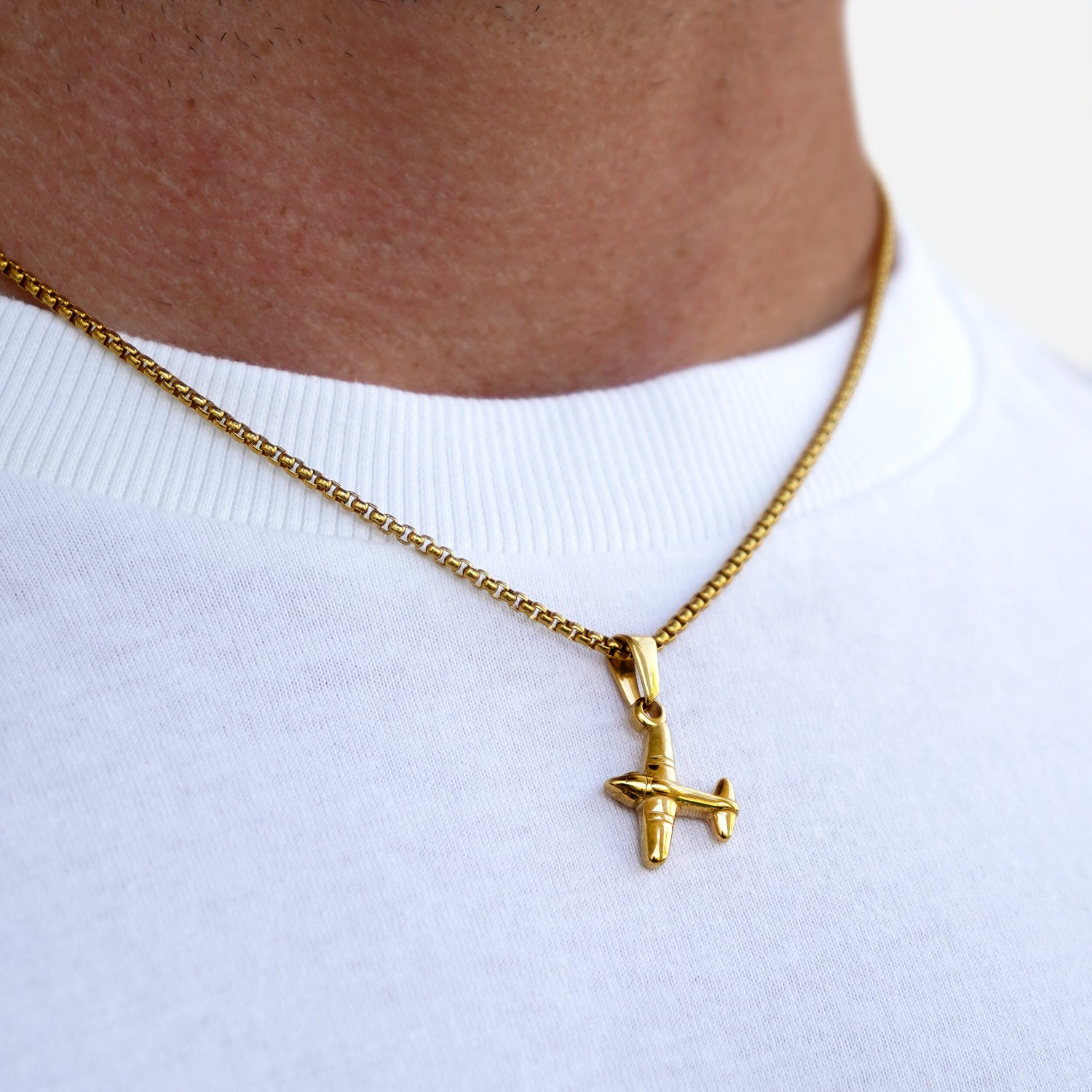 Gold airplane pendant necklace on a white shirt