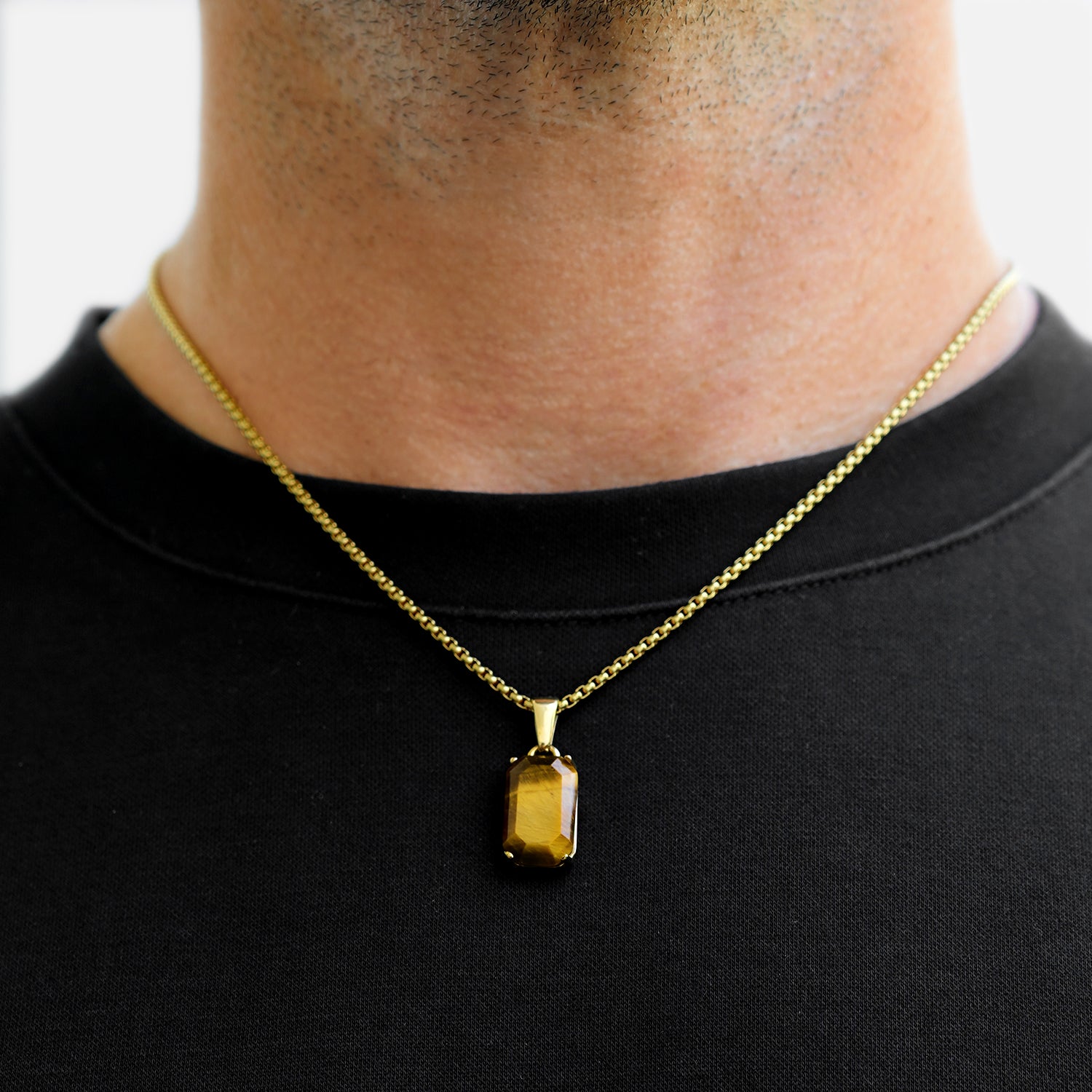 Gold necklace with a pendant worn by a person on a plain background