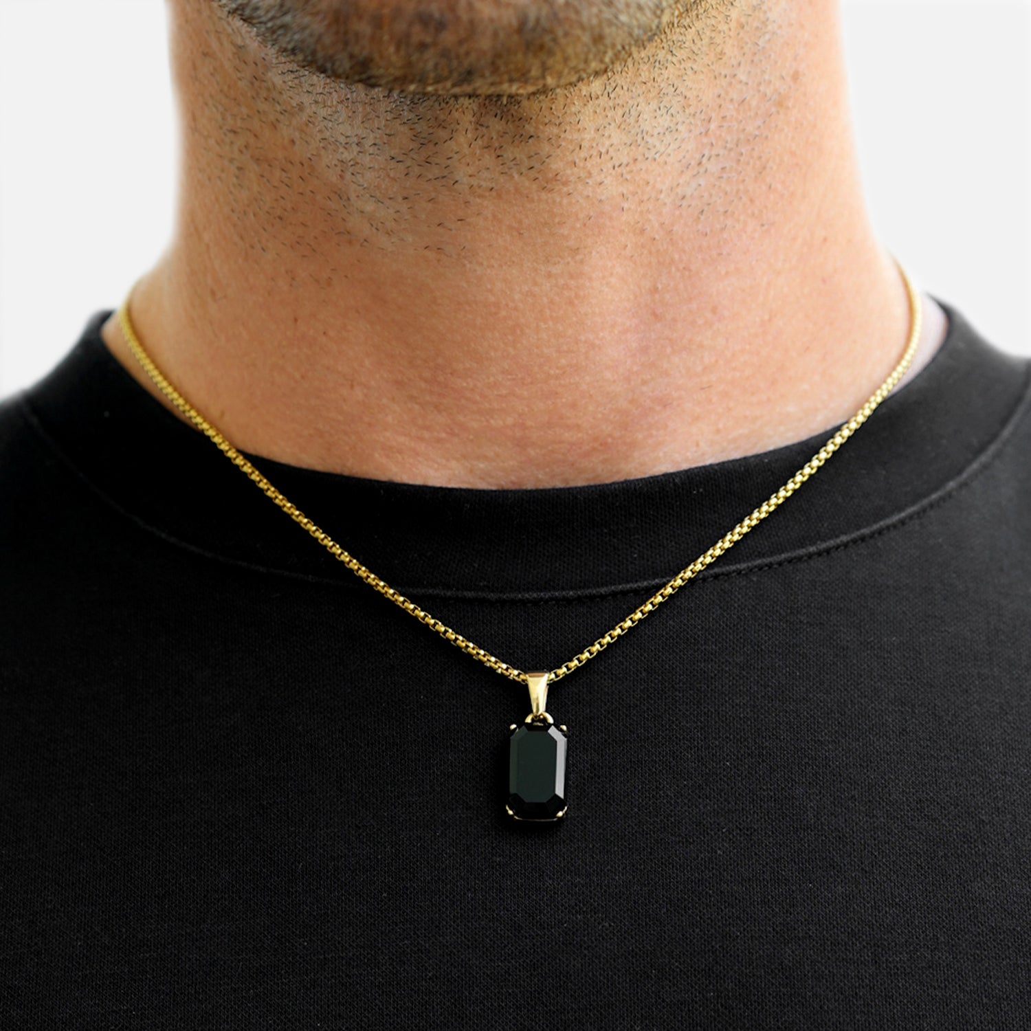 Gold necklace with a black pendant worn by a person against a neutral background