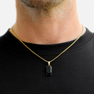 Gold necklace with a black pendant worn by a person against a neutral background