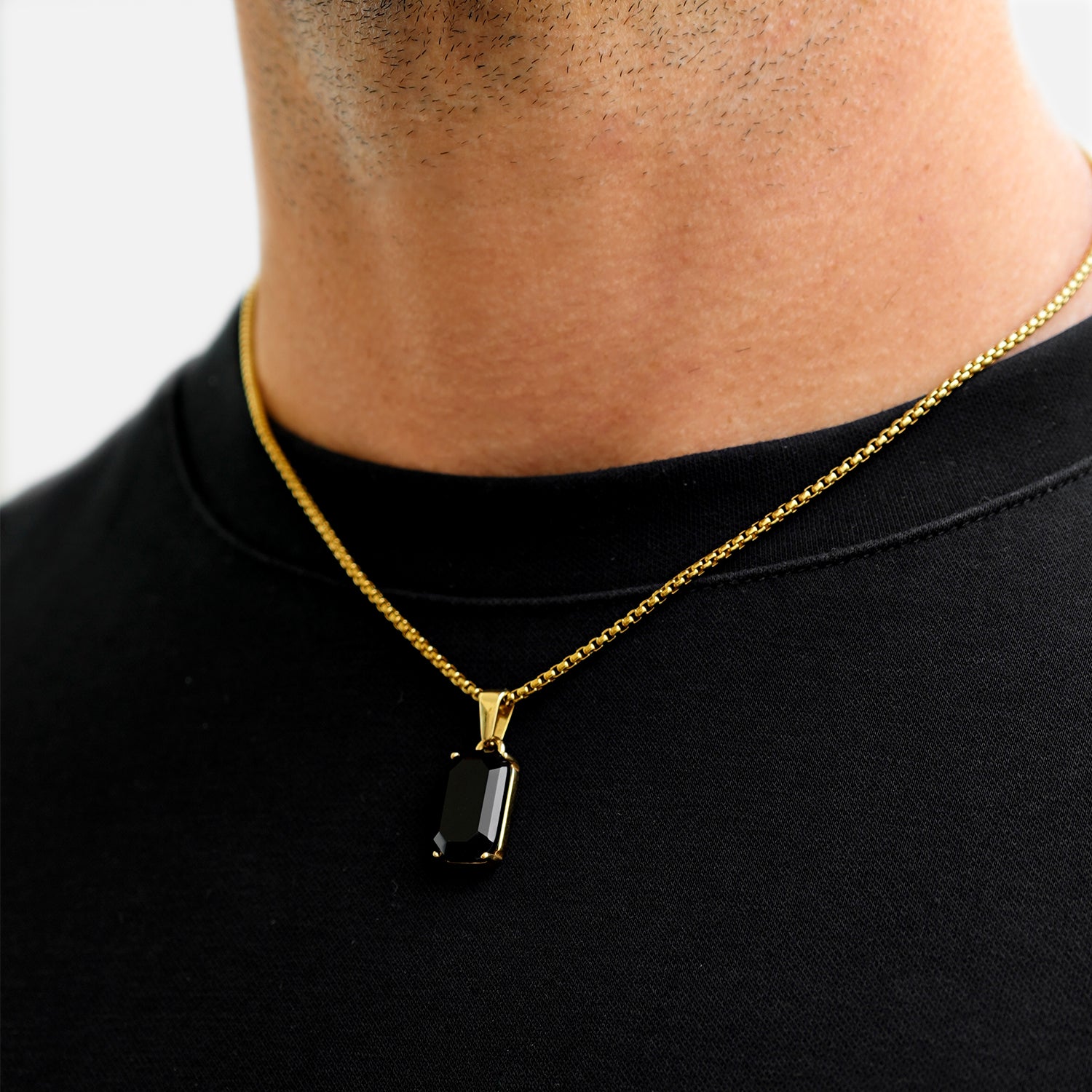 Gold necklace with a black pendant worn by a person on a plain background