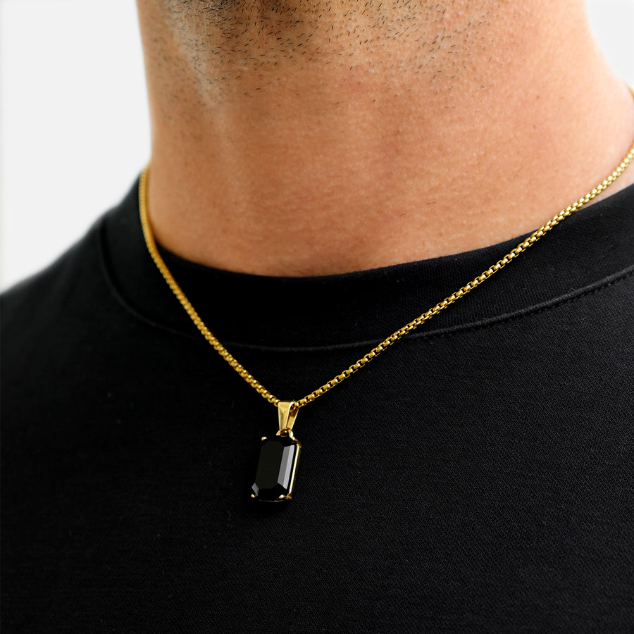 Gold necklace with a black pendant worn by a person on a plain background