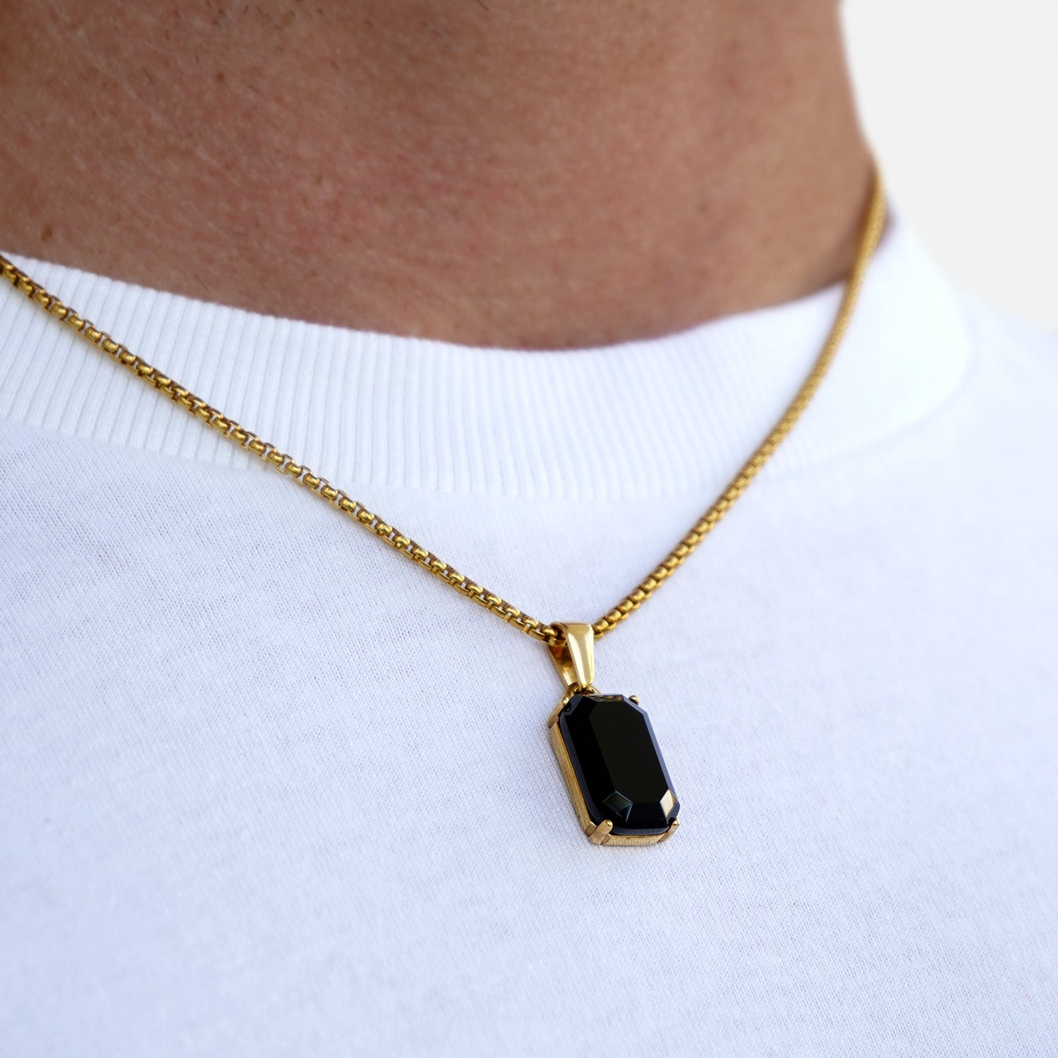 Gold necklace with a black pendant on a white background