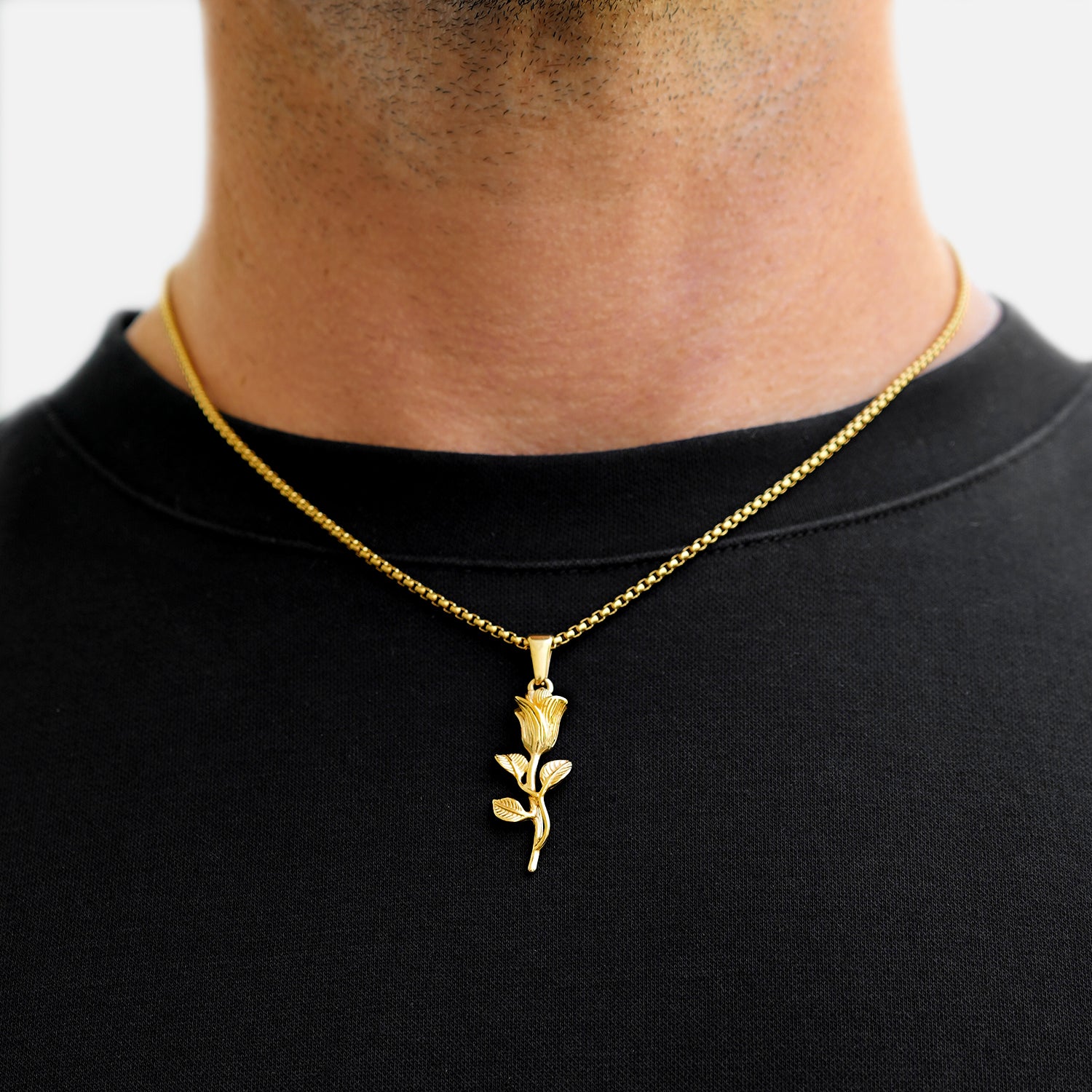 Gold rose pendant necklace on a black shirt against a white background