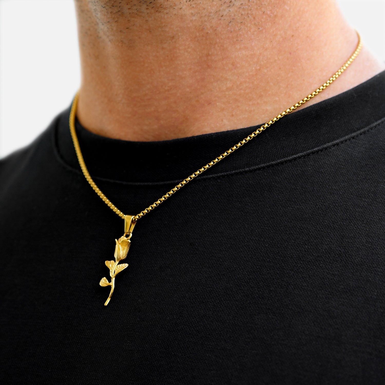 Gold necklace with a leaf pendant worn by a person on a black shirt.