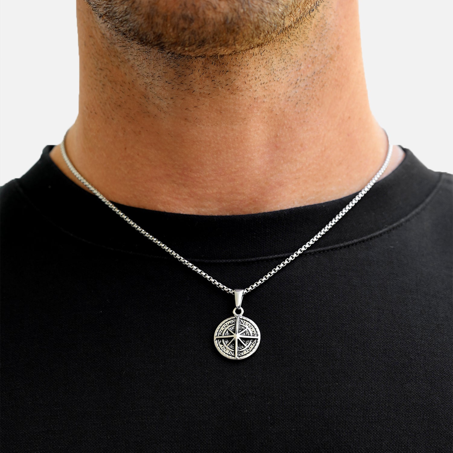 Silver necklace with a circular pendant worn by a person on a plain background