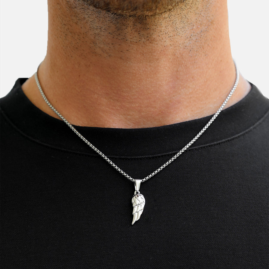 Silver necklace with a feather pendant worn by a person on a plain background