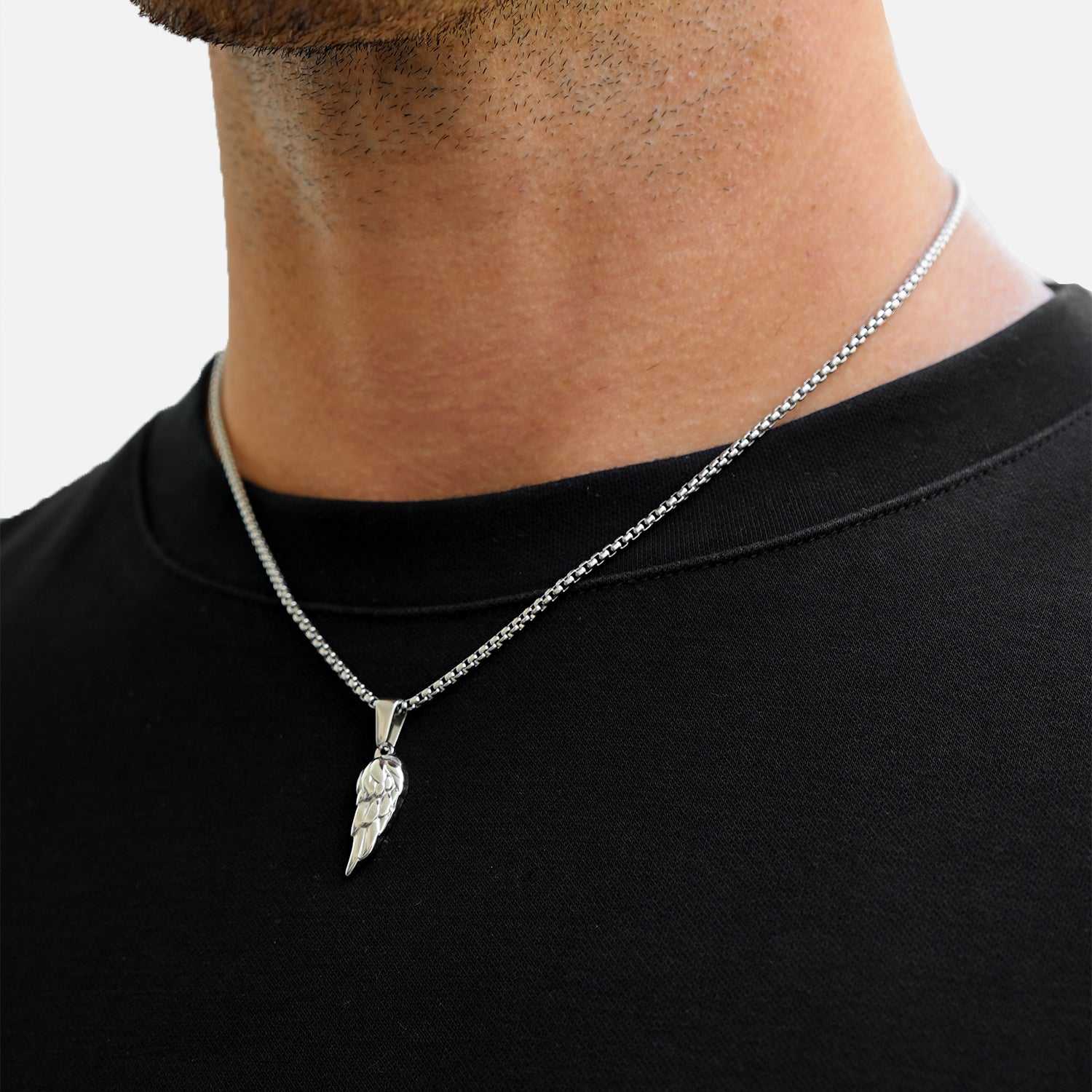 Man wearing a black shirt with a silver necklace featuring a feather pendant.