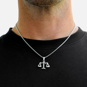 Person wearing a silver necklace with a scale pendant on a plain background