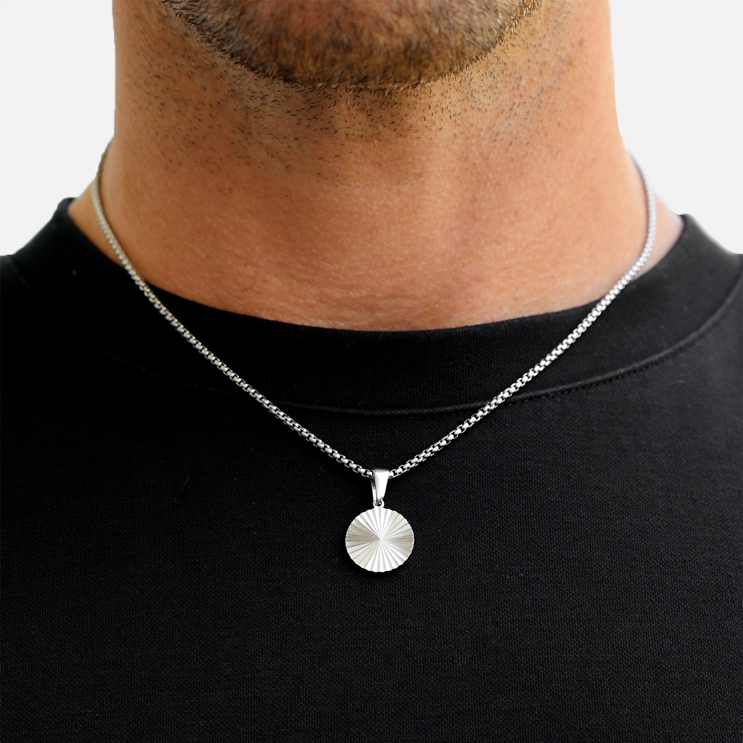 Silver necklace with a round pendant worn by a person on a plain background