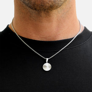 Silver necklace with a round pendant worn by a person on a plain background