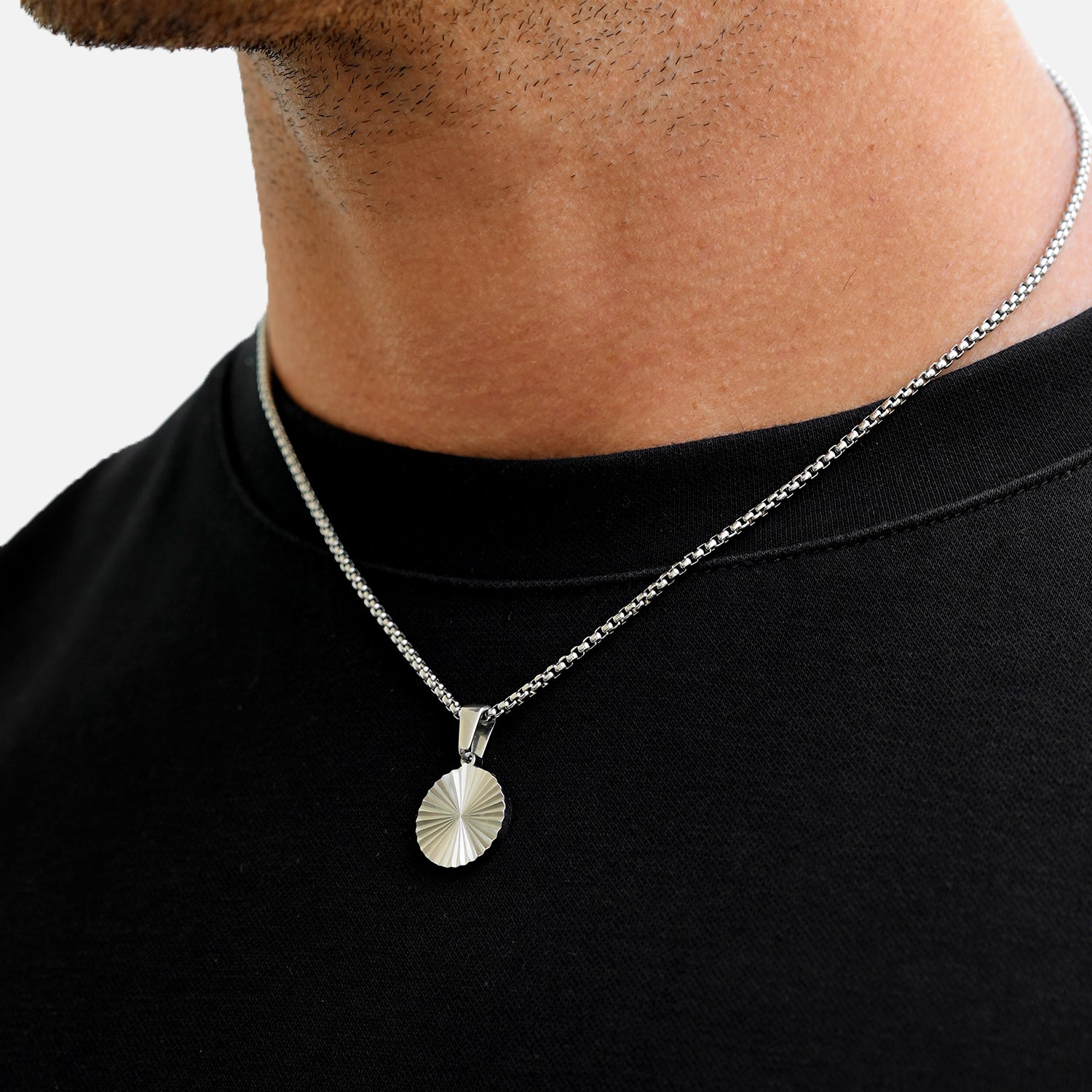 Silver necklace with a round pendant worn by a person on a plain background