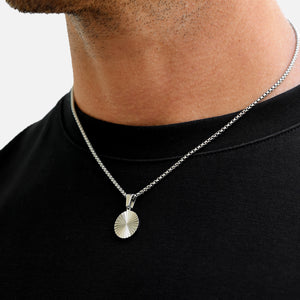 Silver necklace with a round pendant worn by a person on a plain background