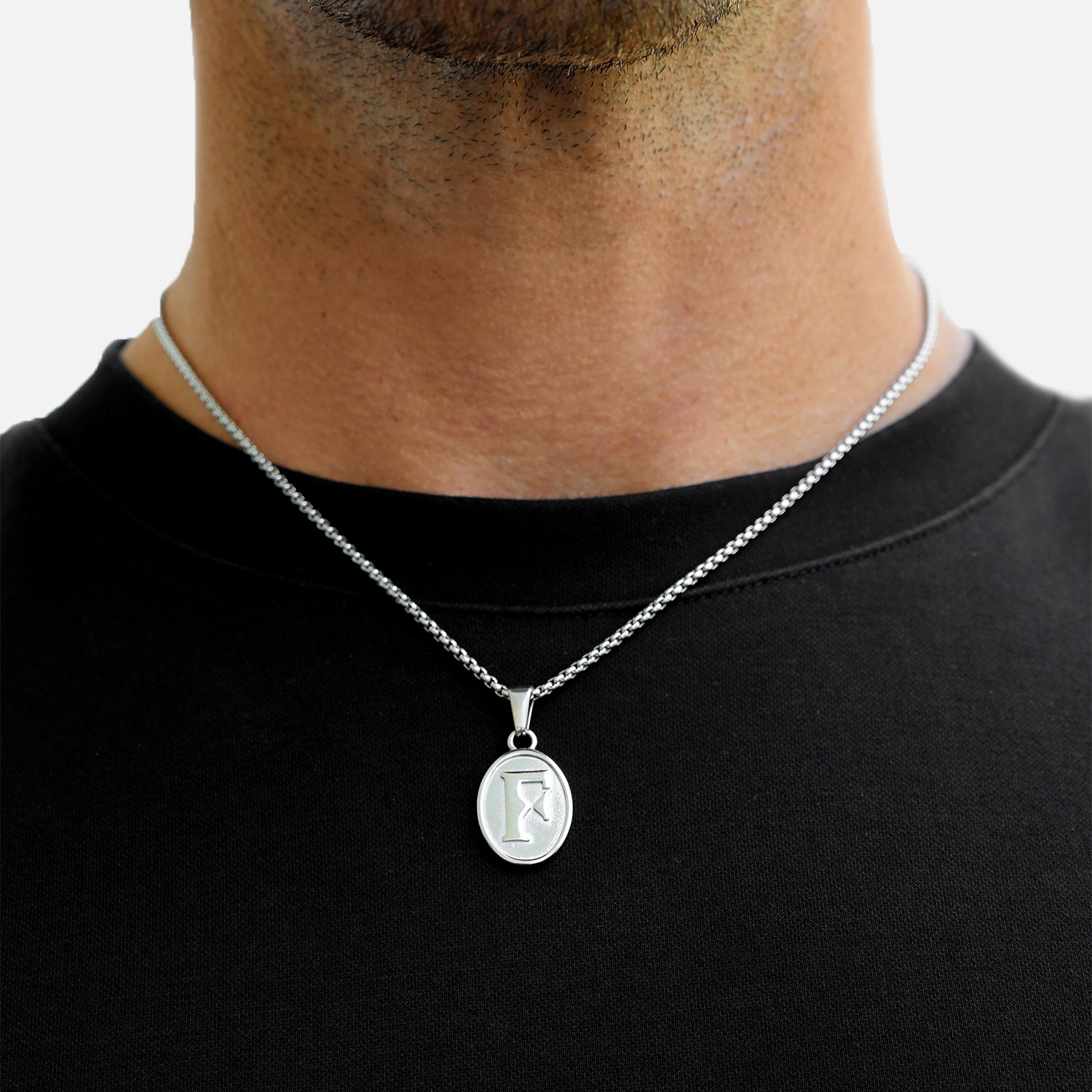 Silver necklace with a pendant worn by a person on a plain background